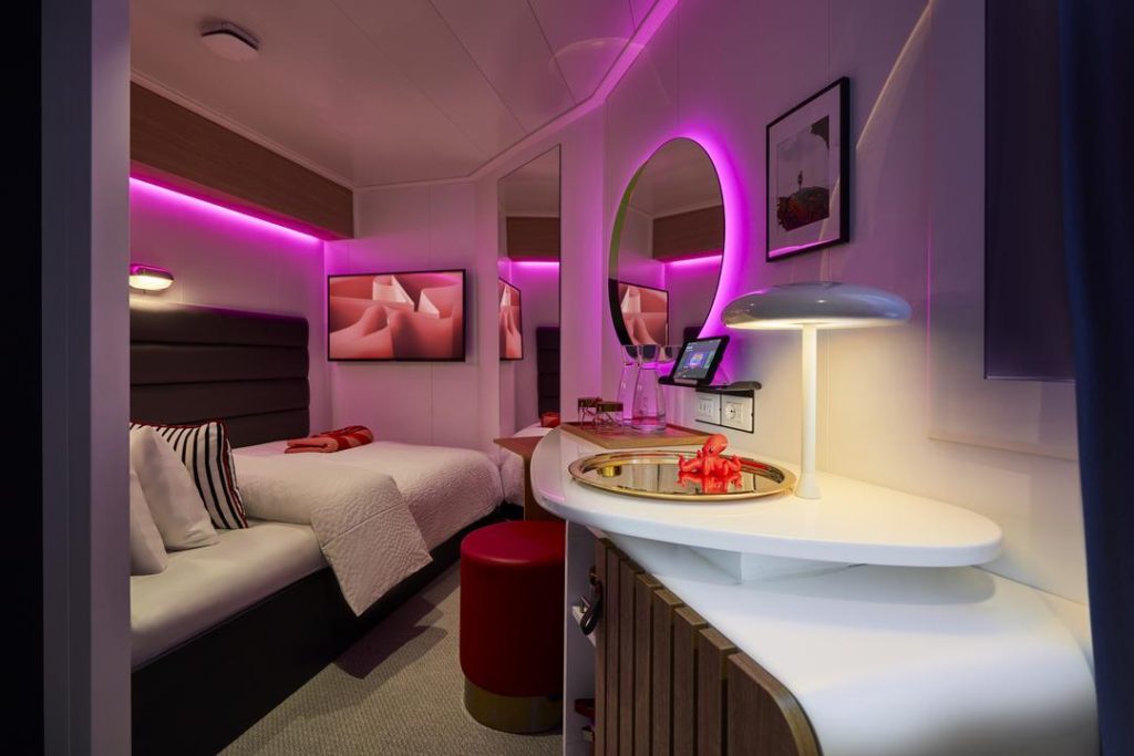 Virgin Voyages Solo Sea View cabin with single bed, vanity and pink mood lighting at night