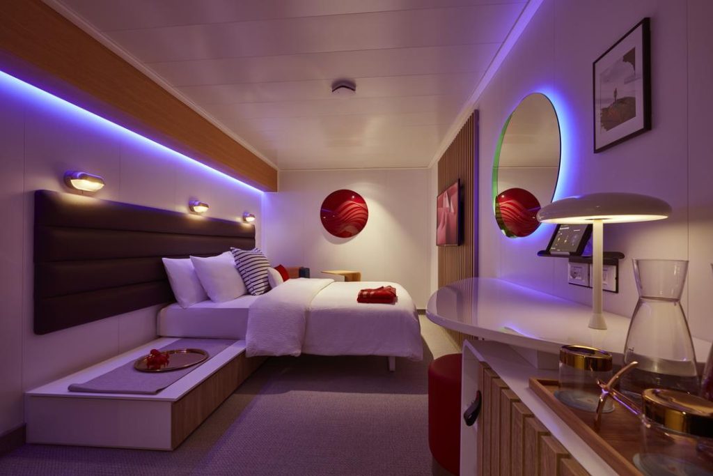 Virgin Voyages Insider cabin with sofa bench, vanity and round mirror under purple mood lighting