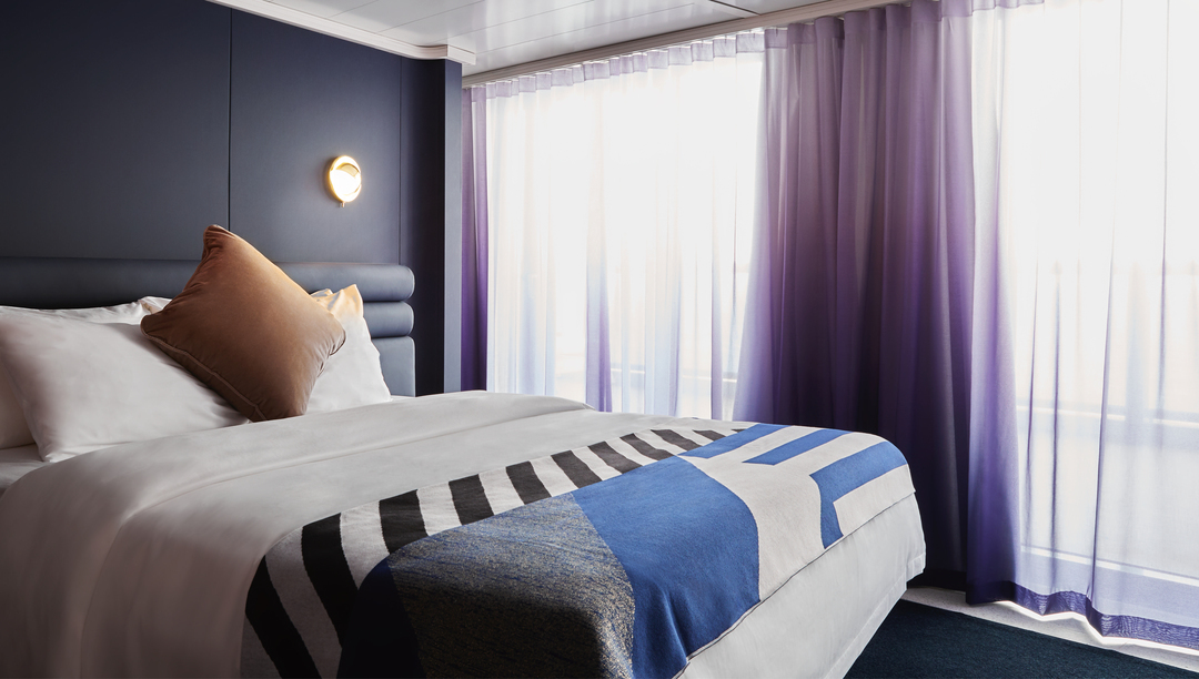 Virgin Voyages Fab Suite bedroom with king bed, purple drapes and contemporary décor