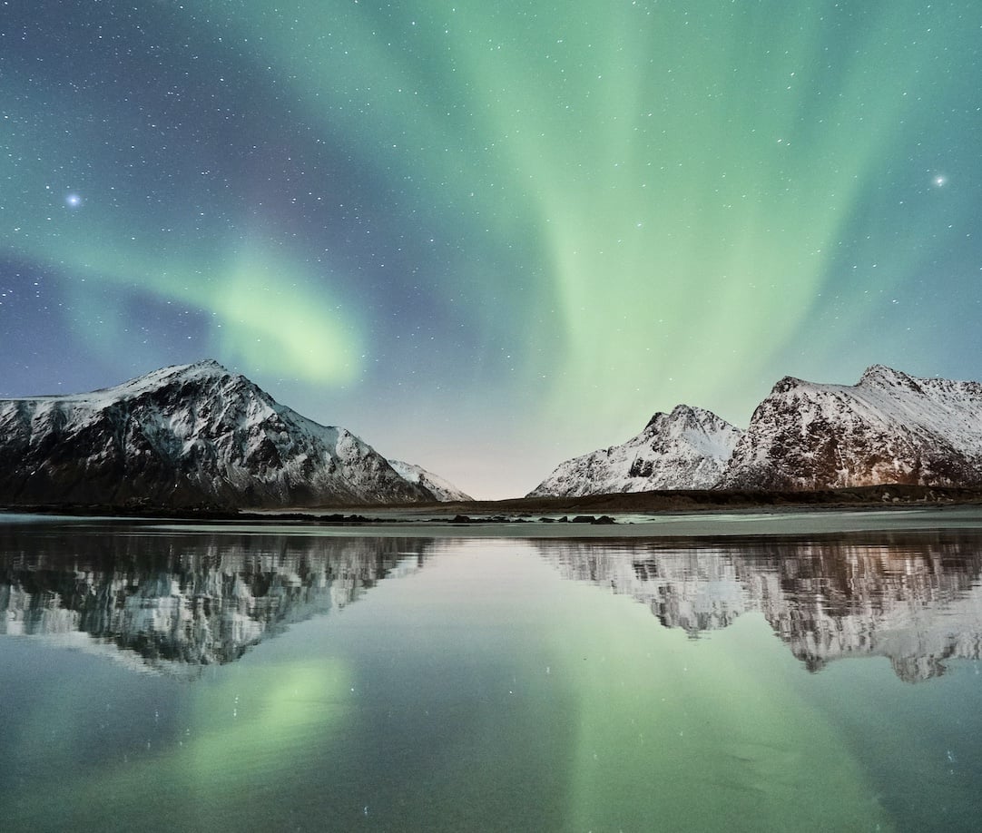 The northern lights over snow-covered Norwegian mountains, reflected in still water