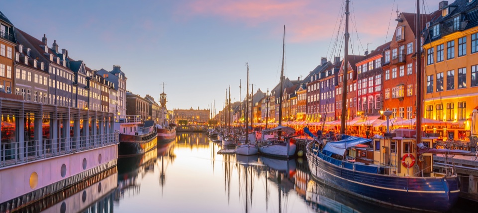 Nyhavn in Copenhagen at sunset, with moored boats and coloured townhouses reflected in the canal